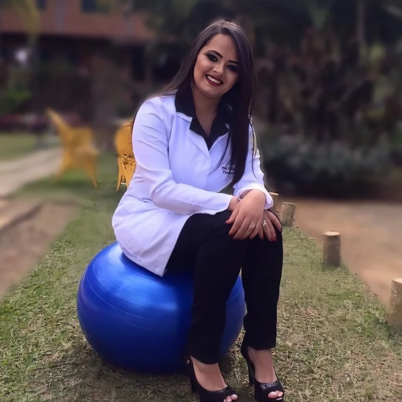 Natália Tomazia sentada em uma bola de exercícios, de jaleco branco, sorrindo